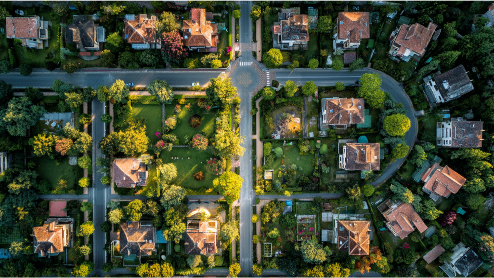 An overhead view of a grid-style suburban area with individual homes, gardens, and tree-shaded yards.