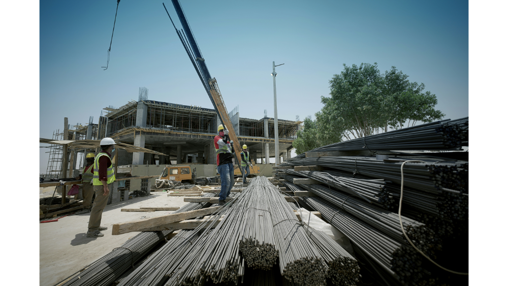 Construction crew members in safety vests and helmets organizing long steel rods with an unfinished concrete building in the background.