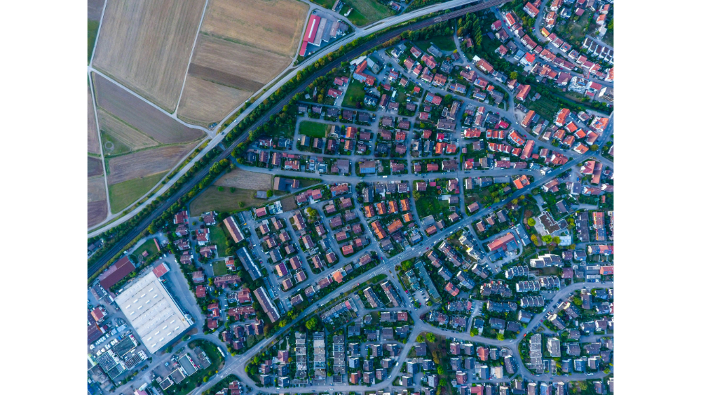 Aerial view of a suburban neighborhood surrounded by farmland, featuring dense housing and curved roads.