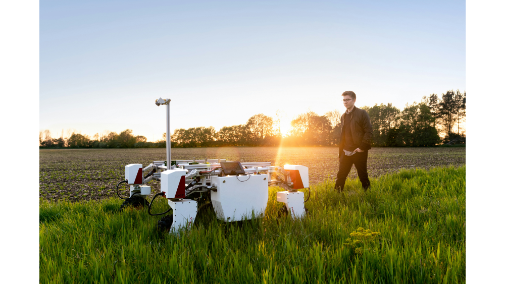 Engineer standing in a grassy field next to a white agricultural robot at sunset, showcasing modern farming technology